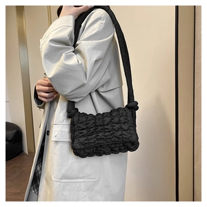 Detail der schwarzen gesteppten Nylon-Schultertasche am Modell mit schickem beigem Trenchcoat