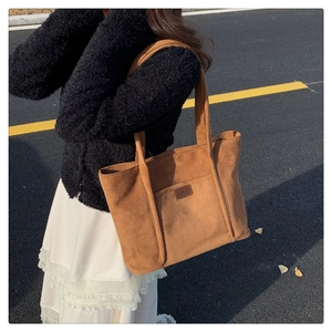 Detailed view of brown suede shoulder bag with front pocket and contrast logo patch
