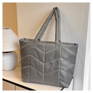 Close-up of grey quilted nylon tote bag with V-shaped stitching on a white cabinet