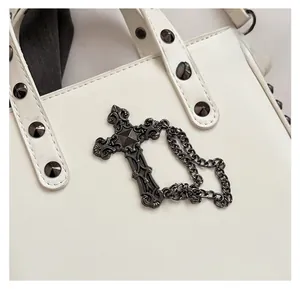 Detail of gothic cross bag charm in gun black metal on white leather studded bag