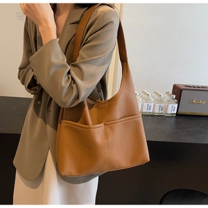 Detail of caramel lychee textured leather hobo bag with dual front pockets and shoulder strap