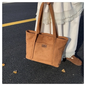 Brown suede tote bag with leather logo detail shown in an autumn street setting