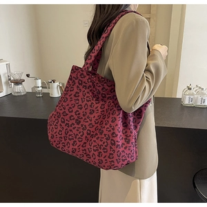Détail du sac cabas en toile à imprimé léopard rouge porté par un mannequin dans un café