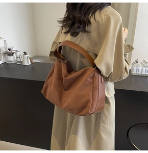 Detailed view of brown suede baguette bag with leather stitching and wide shoulder strap