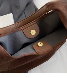 Detailed macro view of the metal magnetic clasp on a brown suede tote bag interior