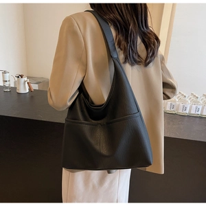 Detail of a black textured PU leather tote bag shown on a model in a minimalist setting