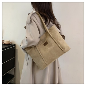 Detail showing khaki suede tote bag with leather logo patch worn by a model