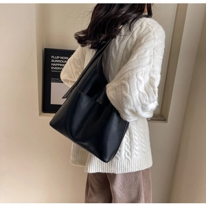 Detail of minimalist black PU leather tote bag with side pocket and wide strap on model