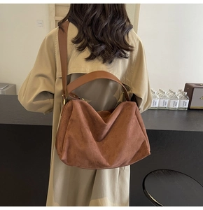 Close-up of brown suede baguette bag featuring wide shoulder strap and metal zipper detail