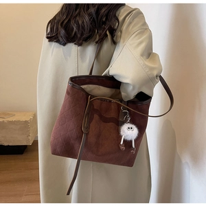 Detail of dark brown quilted suede tote bag with a white plush doll charm accessory