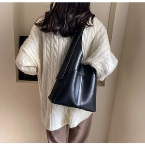 Minimalist black PU leather tote bag worn by model over a soft white knitted sweater