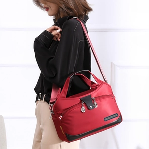 Détail du sac bandoulière en nylon rouge avec anneaux métalliques et écusson Fashion