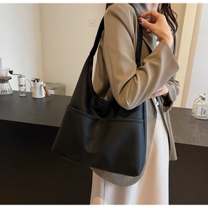 Detail of black textured PU leather tote bag with functional front pockets and wide strap