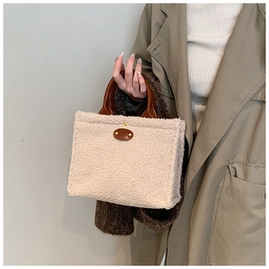 Detail of plush off-white lamb wool tote bag with brown leather handles held by a model