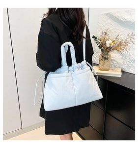 Detail view of light blue quilted shoulder bag with drawstring closure on a model