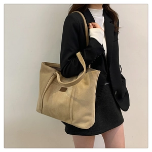 Detailed view of a khaki suede tote bag worn on shoulder by a model in casual office attire