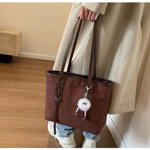 Detail of dark brown quilted velvet tote bag featuring a plush eye doll and leather handles