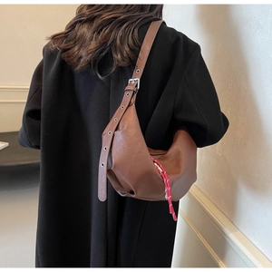Close-up of brown PU leather crescent bag featuring metallic grommeted strap and decorative cord