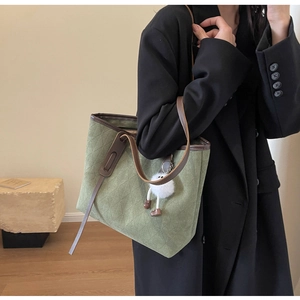 Detail of green quilted velvet tote bag with brown leather straps and plush charm detail