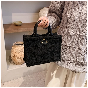 Detail of black faux shearling tote bag with leather handles and gold stud accents