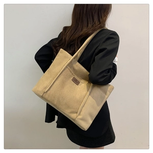 Detail view of khaki faux suede tote bag featuring a leather logo patch on the shoulder strap