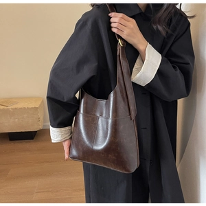 Detail shot of a dark brown PU leather hobo bag worn with a black wool coat