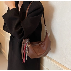 Detail of a brown crescent PU leather bag with metal hardware and decorative pendant charm