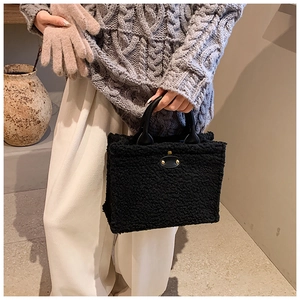 Close-up of black fuzzy plush tote bag with leather handles and metallic rivet detail
