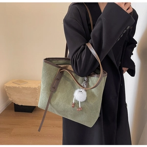 Detail of dark green velvet tote bag with brown leather trim and plush doll accessory
