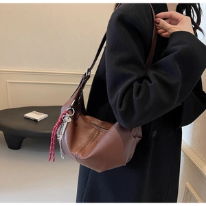 Detail of a brown leather shoulder bag featuring a red woven rope and metal key charm