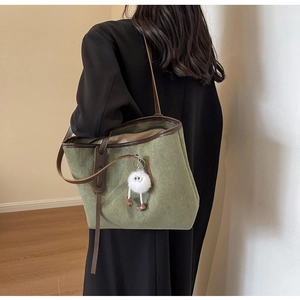 Detailed view of dark green quilted tote bag with brown leather straps and plush charm