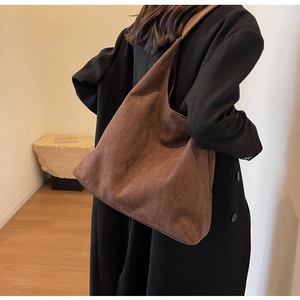 Brown suede tote bag shown on shoulder with black coat for a stylish winter look