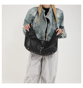 Détail du sac croissant en cuir noir avec boucle en croix argentée et rivets métal