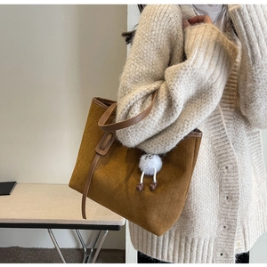 Close-up of brown velvet tote bag with leather handles and cute plush doll keychain charm