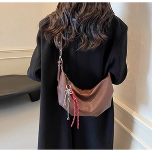 Detail of a brown PU leather half-moon bag featuring a silver key and red cord charm