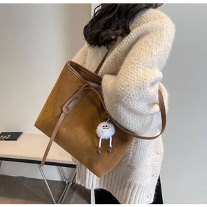 Detail of a brown suede quilted tote bag with a cute plush charm worn by a model