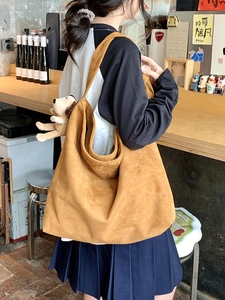 Detail of a large brown suede tote bag featuring a cute plush puppy charm accessory