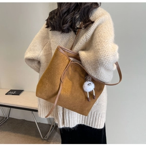Brown quilted velvet tote bag with creative white plush charm in a minimalist studio setting
