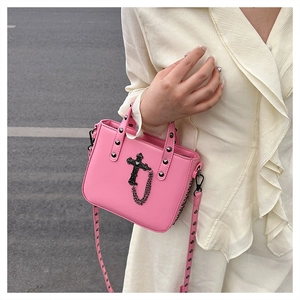Close-up of pink PU crossbody bag with black rivets, cross pendant, and chain detail