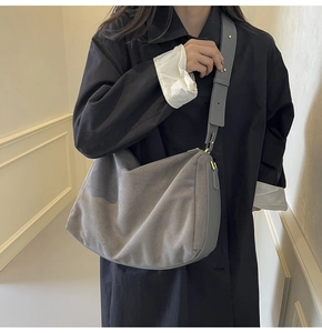 Model wearing a grey suede hobo bag with gold metal buckles in a minimalist interior