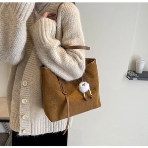 Detail of a brown suede tote bag with quilted pattern and a white plush toy charm