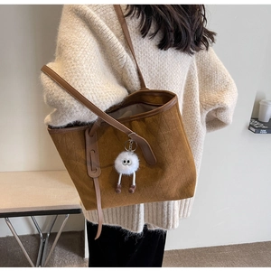 Detail of brown quilted velvet tote bag with a cute white furry monster bag charm pendant