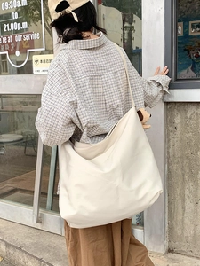 Side view of a large cream canvas hobo bag with a cute brown doll charm detail