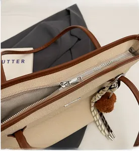 Detailed close-up of beige canvas tote bag with brown leather trim and silver metal zipper