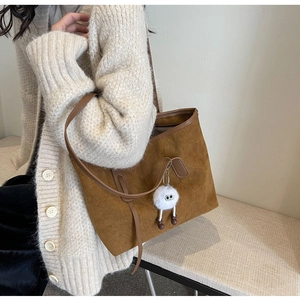 Close-up of a large brown suede tote bag featuring a cute white plush doll accessory