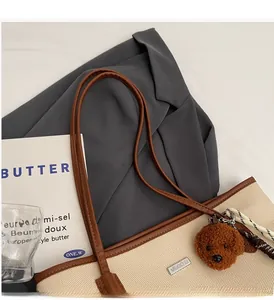 Detail of beige canvas tote with brown leather handles and a plush teddy bear charm