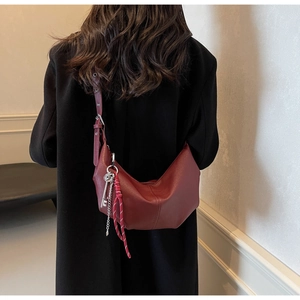 Detail of burgundy half-moon crossbody bag featuring decorative metal key and woven rope