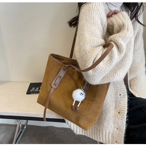 Detail of brown suede tote bag featuring diamond stitching and cute plush monster charm