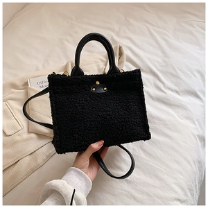 Fashionable black faux shearling shoulder bag with leather handles and gold metal accents