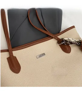 Detail of canvas tote bag showing brown leather trim and metallic brand logo plate